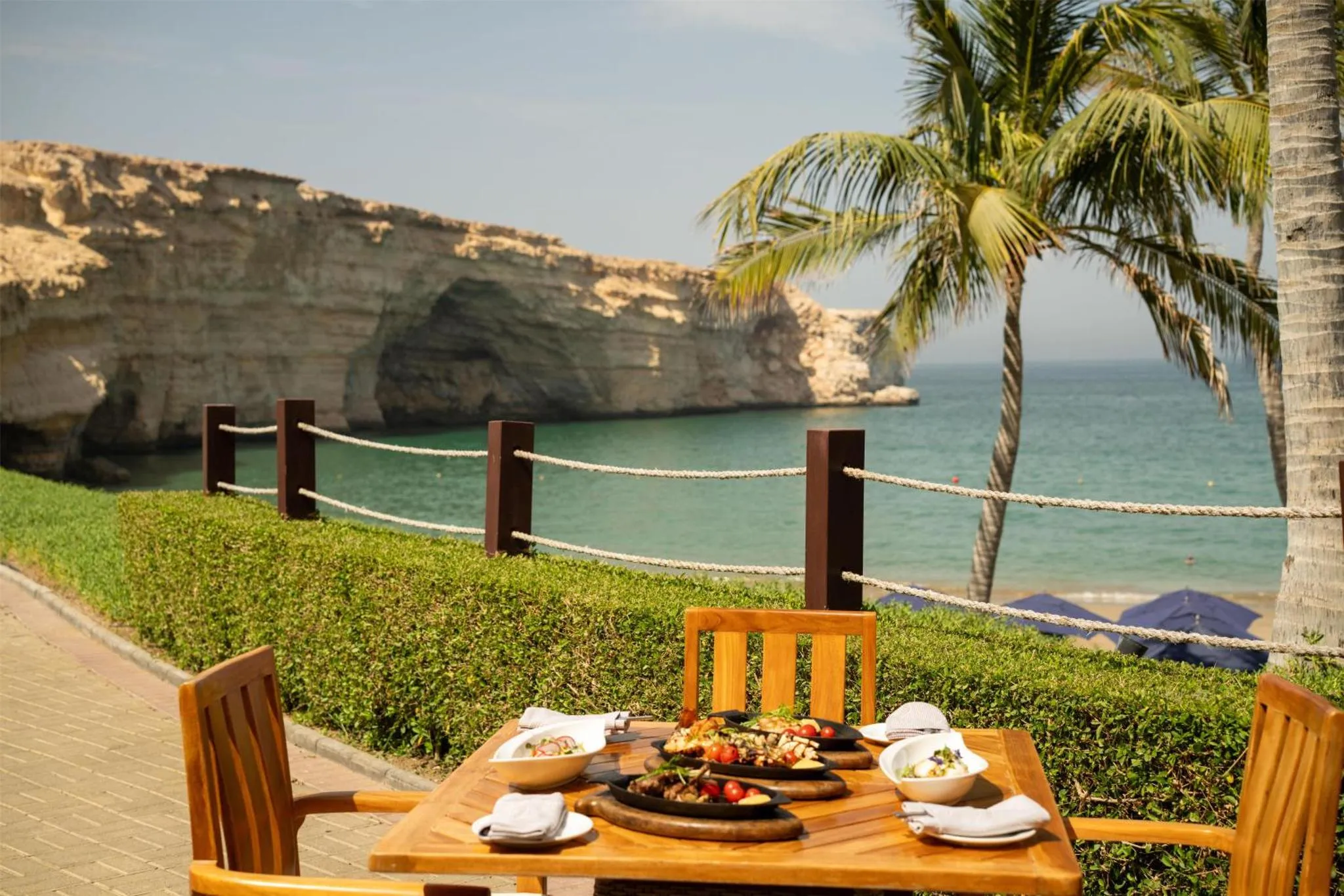 Une table est dressée avec des plats servis en extérieur, face à une crique bordée de falaises.