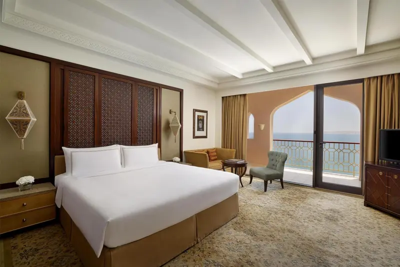 Chambre lumineuse avec un grand lit et un coin salon donnant sur la mer.