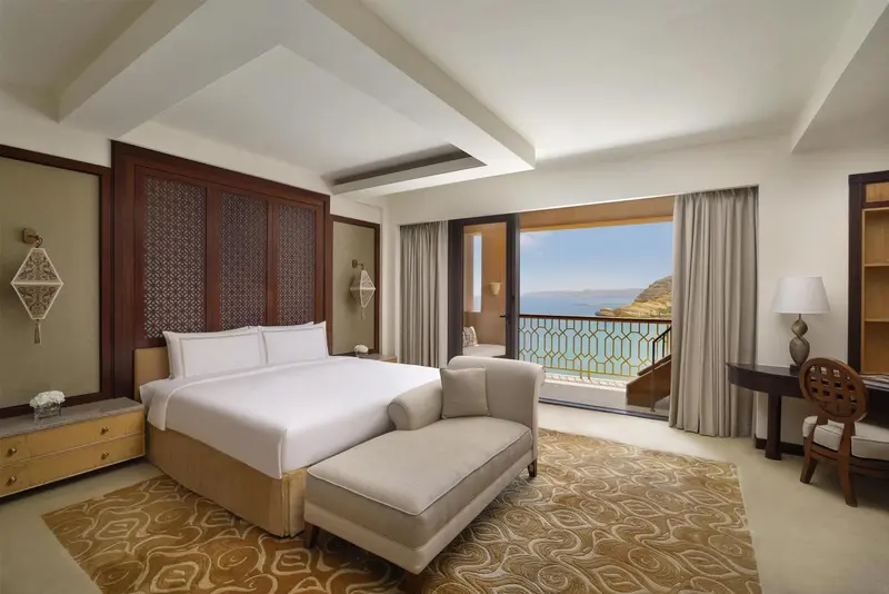 Chambre lumineuse avec un grand lit et un accès à un balcon avec vue sur la mer.