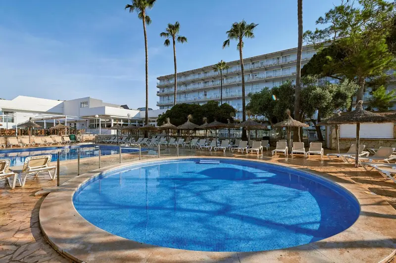 Piscine rectangulaire et bassin circulaire devant un bâtiment à plusieurs étages bordé de palmiers.