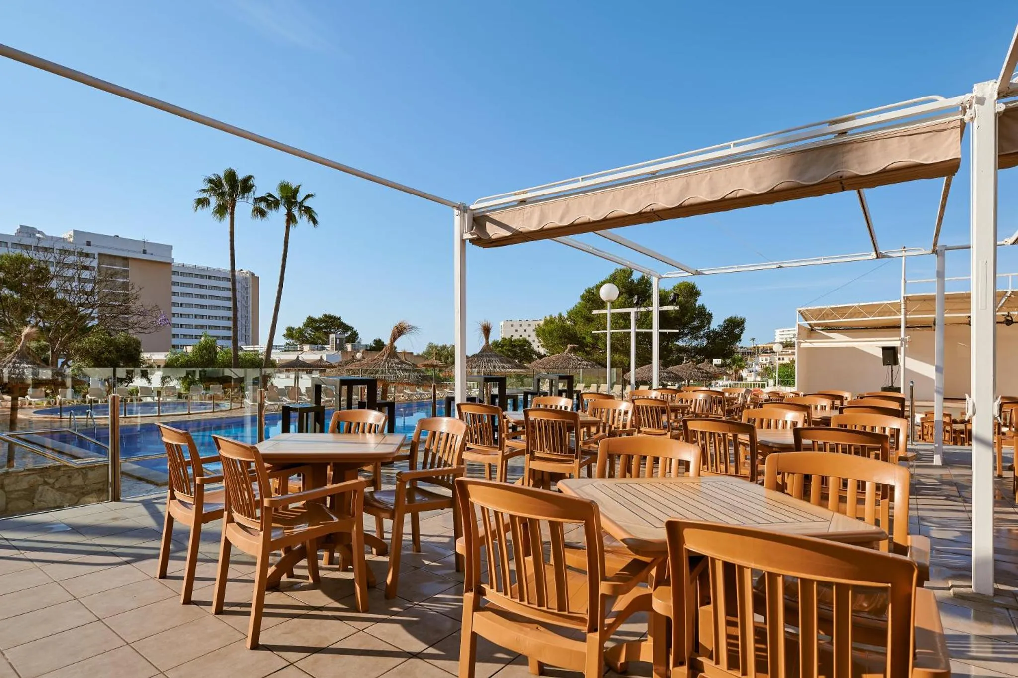 Terrasse ombragée avec tables et chaises près d'une piscine.