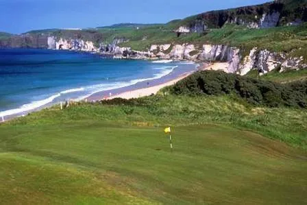 Cote rocheuse et plage de sable fin bordant une eau turquoise.