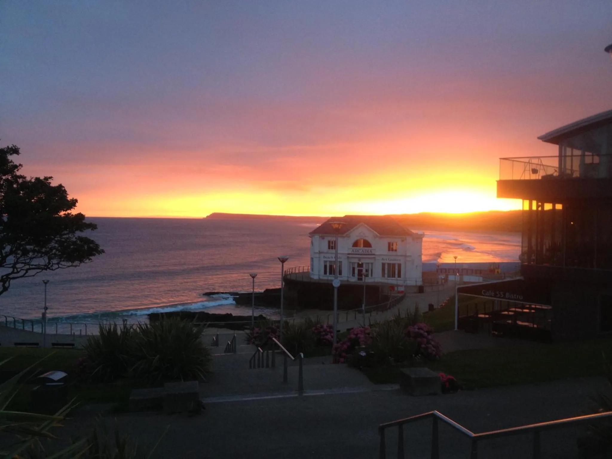 Coucher de soleil sur l'océan avec un bâtiment au premier plan et une promenade.