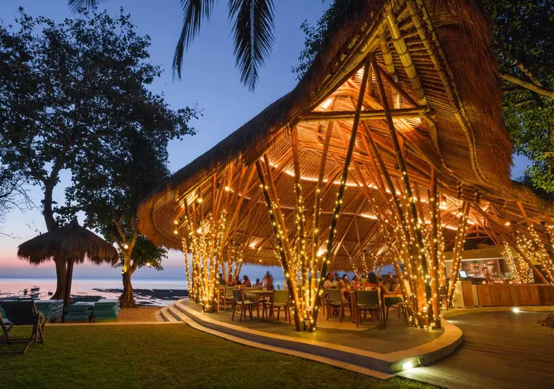 Une salle à manger ouverte sur une plage au coucher du soleil.