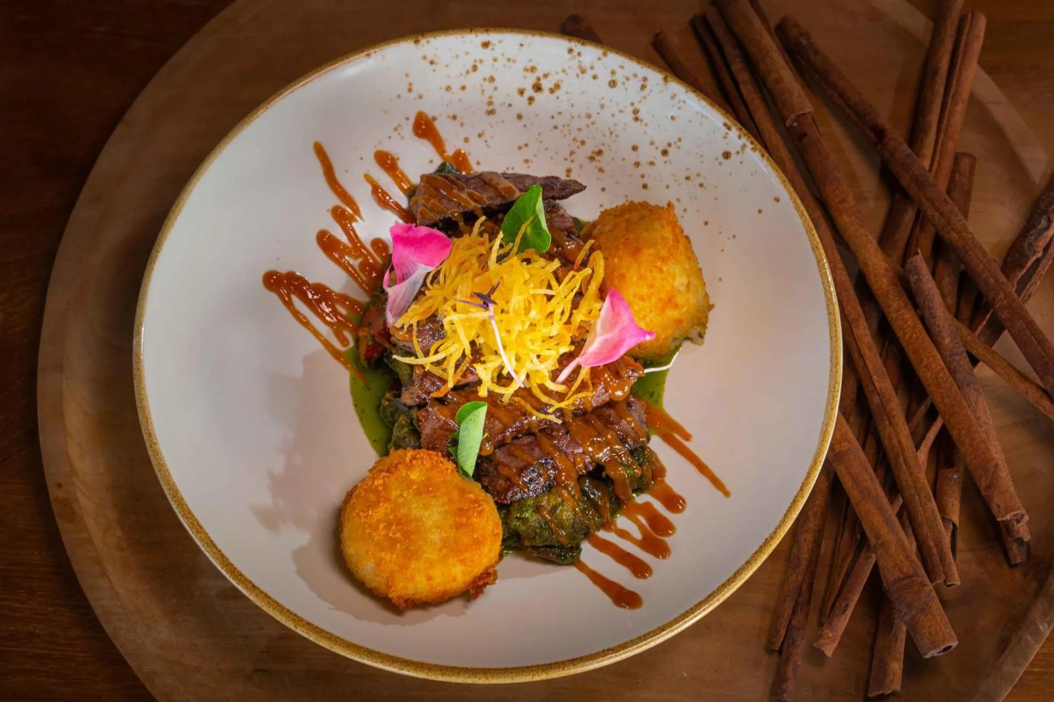 Assiette de viande accompagnée de légumes, de sauce et de bâtonnets de cannelle.