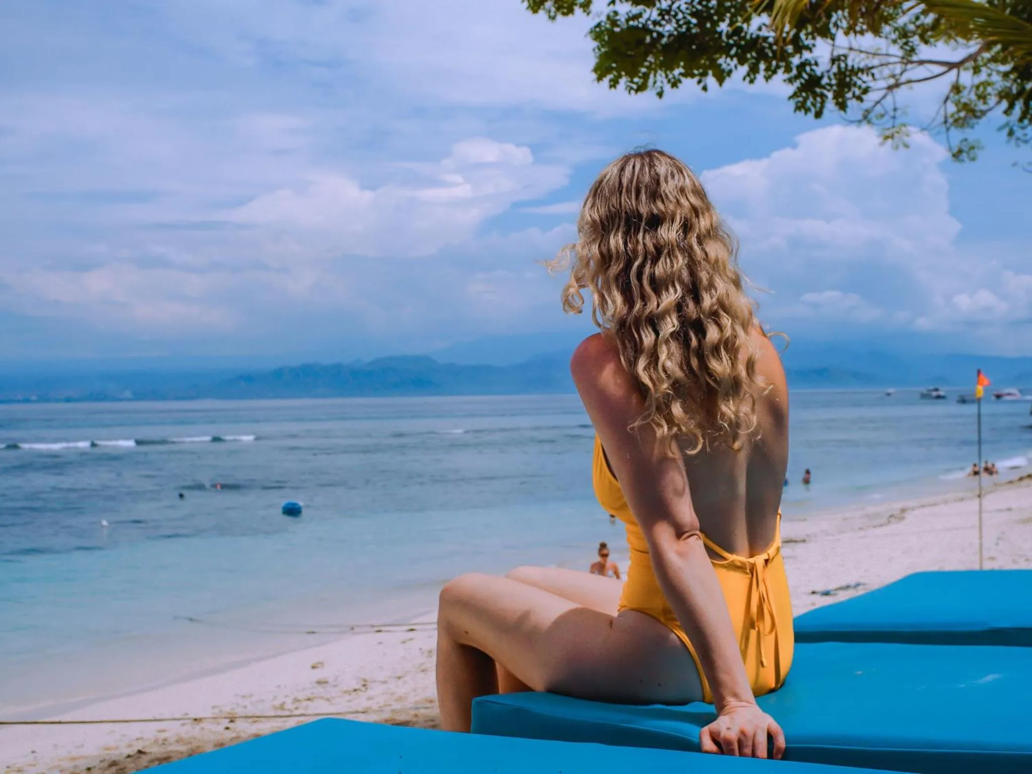Une femme assise sur un transat bleu face à la mer.
