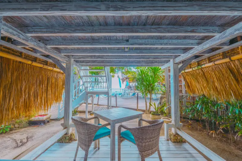 Une table et deux chaises se trouvent sous une pergola en chaume.