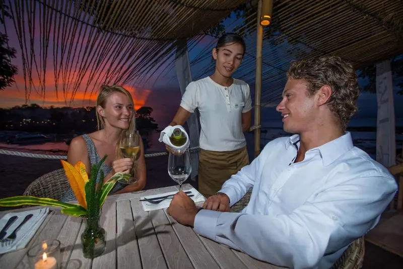 Un couple déguste du vin au coucher du soleil sur une plage.