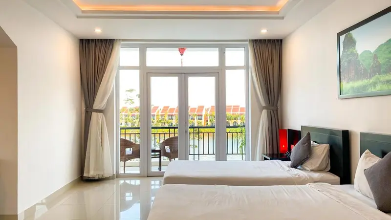 Une chambre lumineuse avec deux lits simples et un balcon donnant sur un paysage verdoyant.