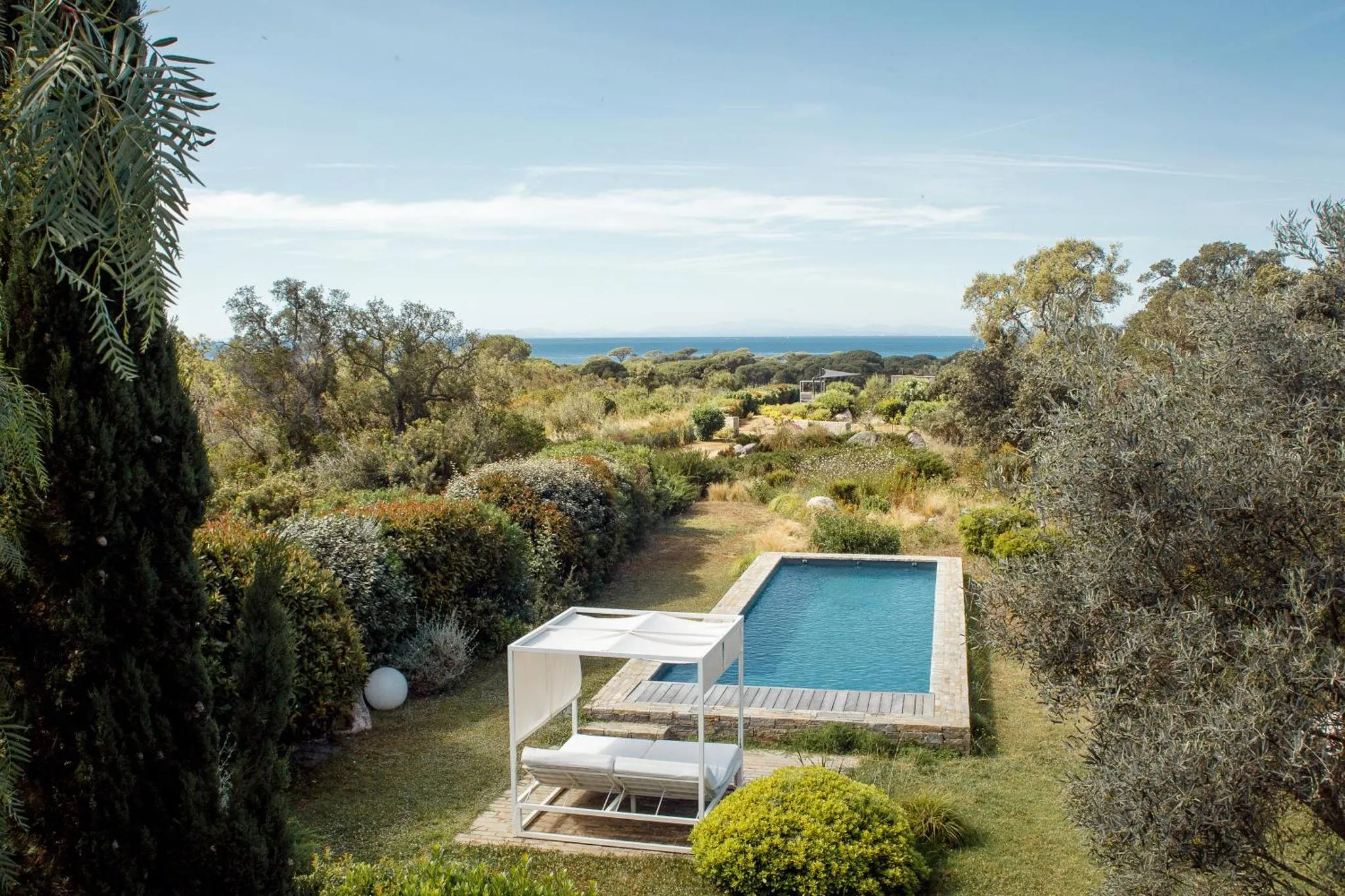 Une piscine rectangulaire avec des transats blancs et une vue sur la mer.