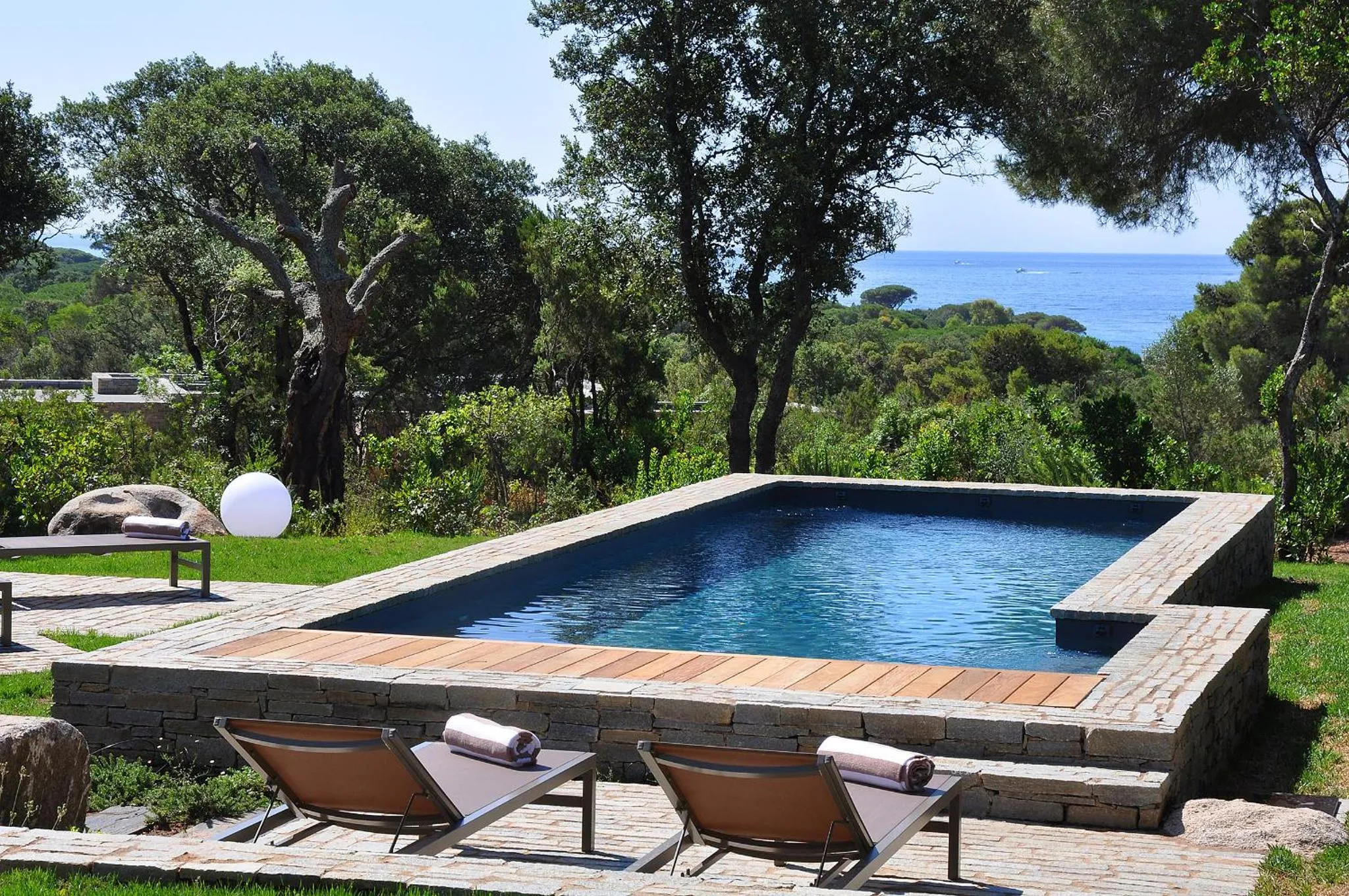 Deux transats sont placés au bord d'une piscine rectangulaire entourée d'une terrasse en pierre.
