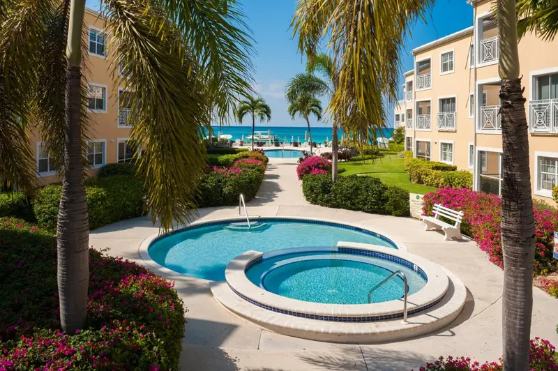 Jardin tropical avec piscine et jacuzzi devant un bâtiment pastel.