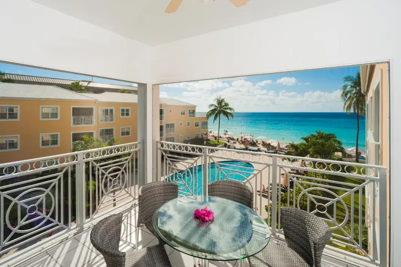 Balcon avec table et chaises donnant sur une vue mer et une piscine.