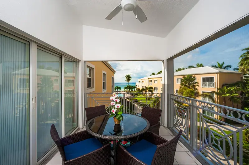 Une terrasse aménagée avec une table et des chaises offre une vue sur la mer et la végétation.