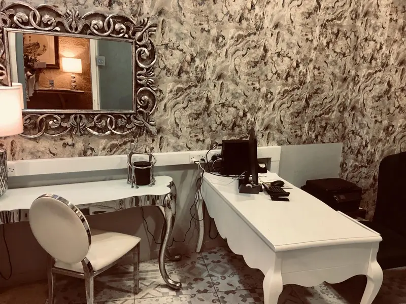 Un bureau blanc avec une chaise face à un miroir décoratif dans une pièce lumineuse.