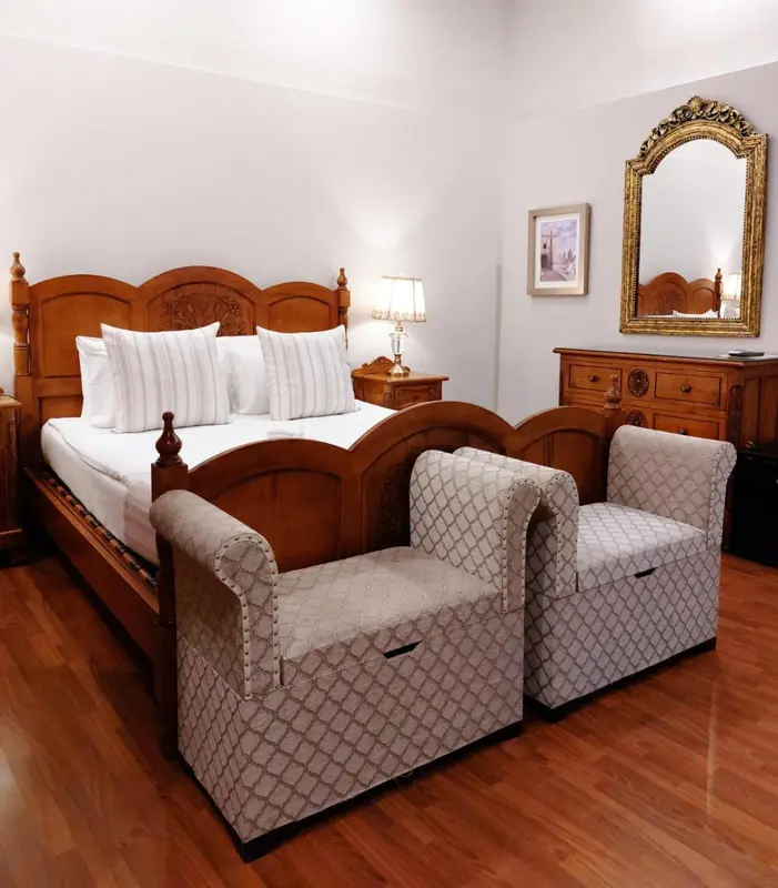 Une chambre lumineuse avec un grand lit en bois et deux fauteuils.