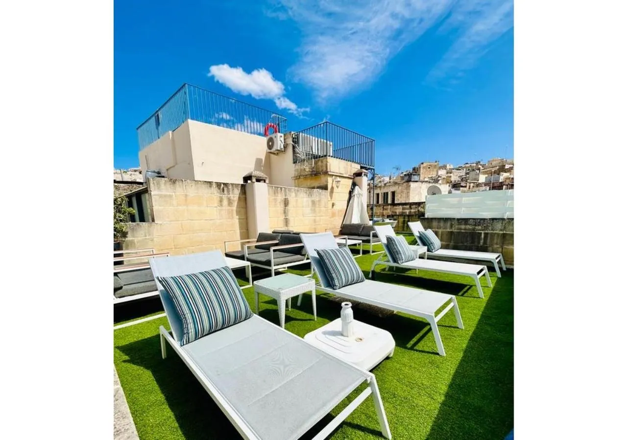 Transats blancs alignés sur une terrasse avec gazon synthétique et vue sur la ville.