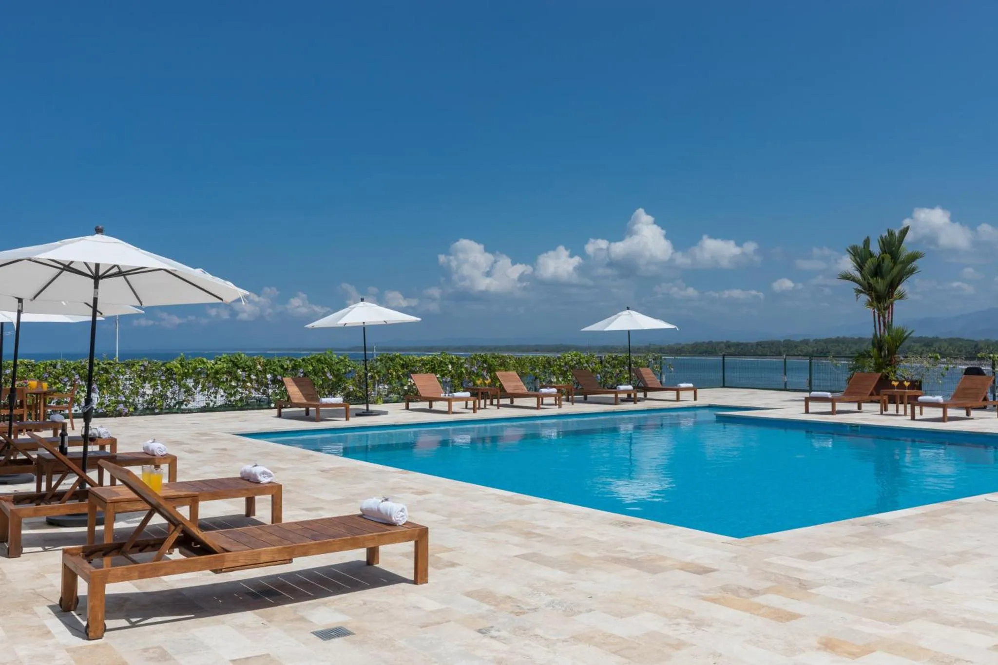 Transats et parasols bordent une piscine turquoise avec vue sur la mer.