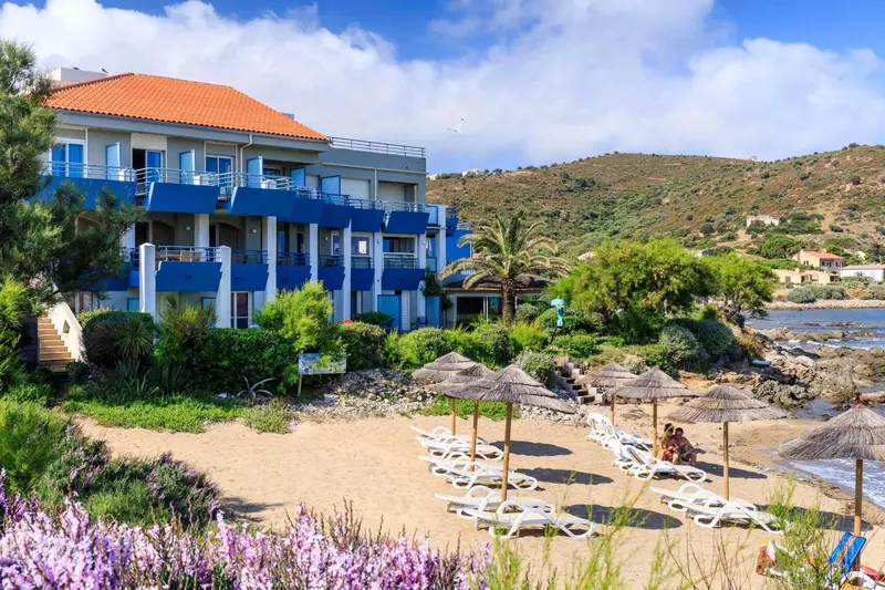 Bâtiment bleu et blanc surplombant une plage de sable avec des parasols.