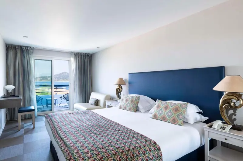 Une chambre lumineuse avec un grand lit et un balcon donnant sur la mer.