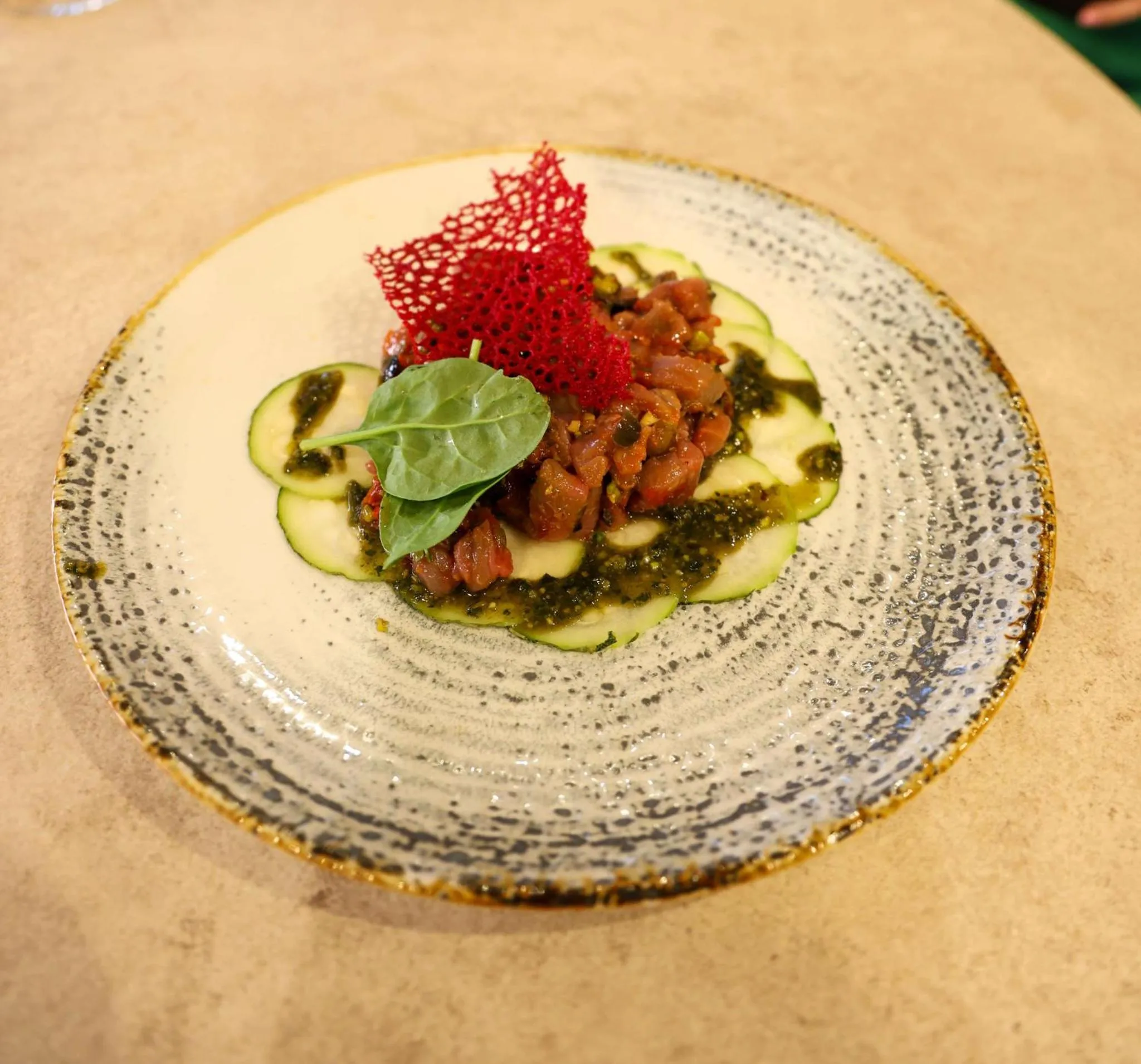 Assiette ornée d'une préparation culinaire à base de poisson cru, de légumes et d'une sauce verte.