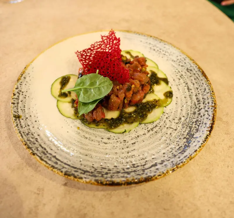 Assiette ornée d'une préparation culinaire à base de poisson cru, de légumes et d'une sauce verte.