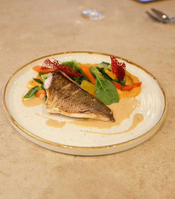 Assiette de poisson grillé avec légumes et sauce.