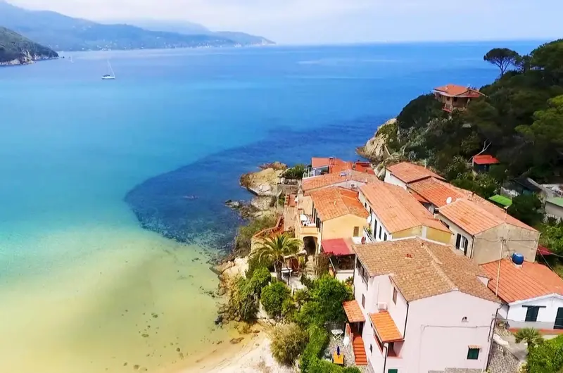 Vue aérienne d'un village côtier avec des bâtiments aux toits rouges et une plage.