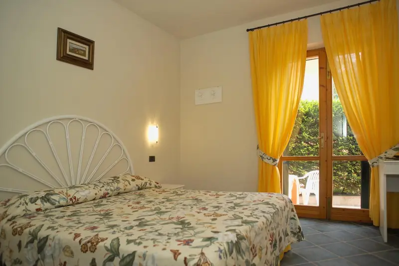 Une chambre lumineuse avec un lit recouvert d'une couette fleurie et des rideaux jaunes.