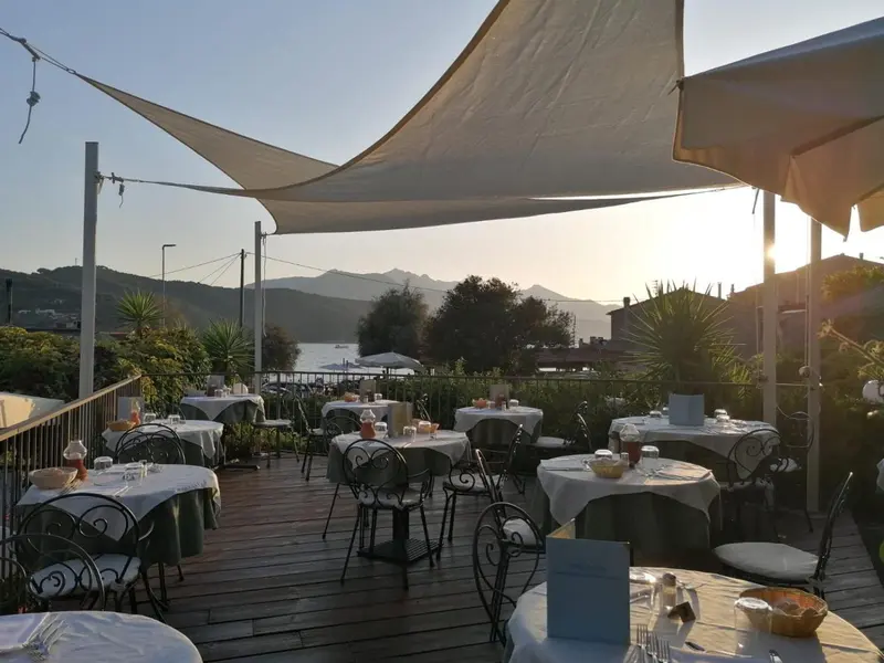 Terrasse ombragée avec tables nappées face à un paysage côtier.