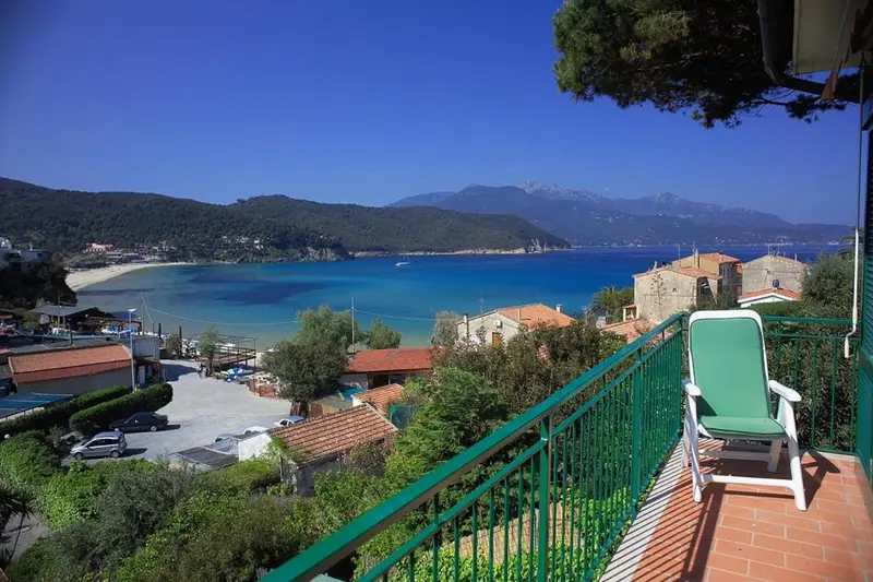 Vue d'une terrasse avec transat donnant sur une crique et des collines.