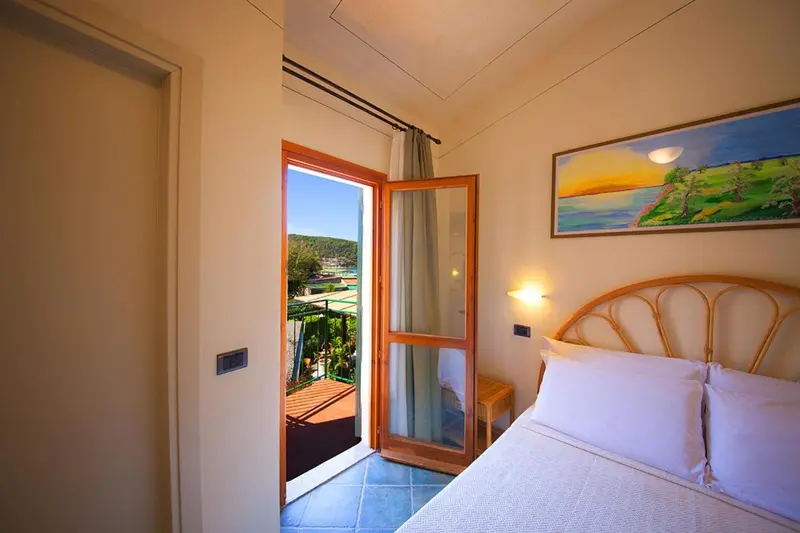Une chambre lumineuse s'ouvre sur un balcon avec vue sur la végétation.