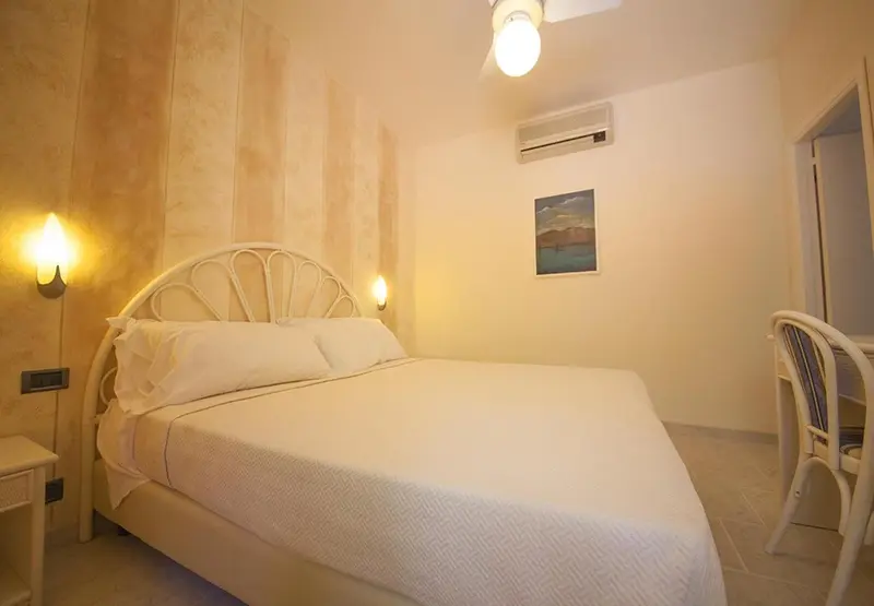 Une chambre lumineuse avec un grand lit blanc et des appliques murales.