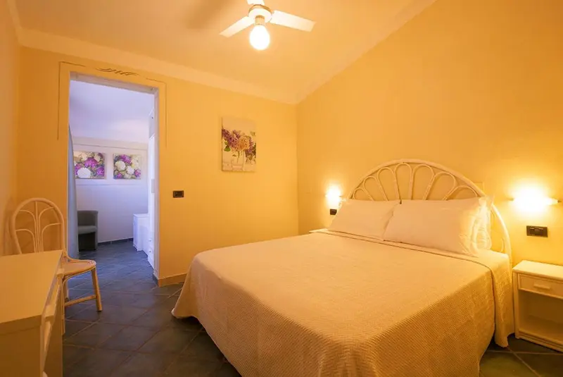Une chambre lumineuse avec un lit recouvert d'une couverture blanche et un tableau floral.