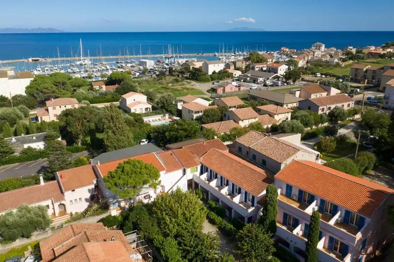 Vue aérienne d'un ensemble de bâtiments aux toits en tuiles rouges surplombant un port de plaisance et la mer.