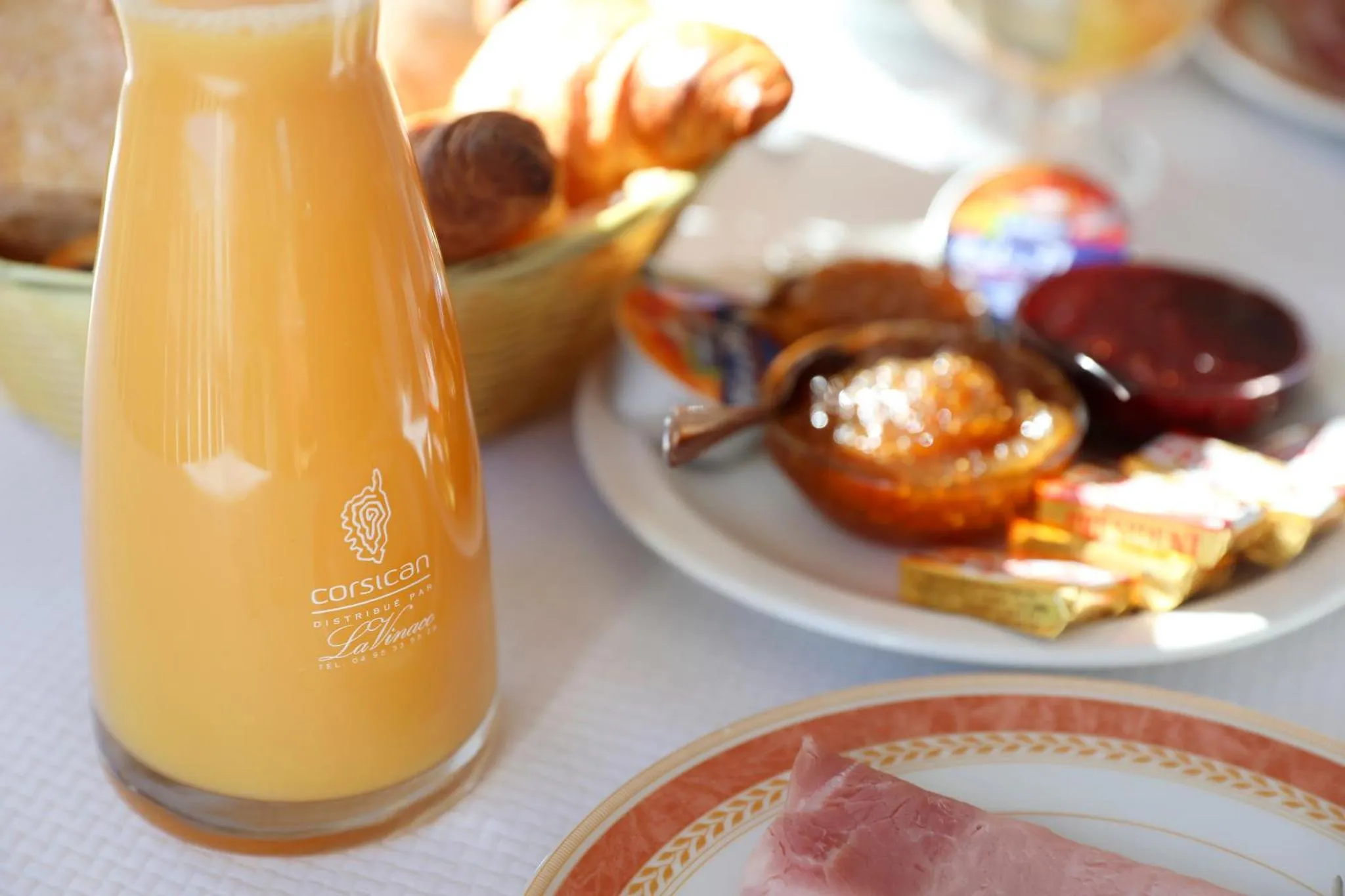 Une table est dressée avec des viennoiseries, de la confiture et une carafe de jus d'orange.
