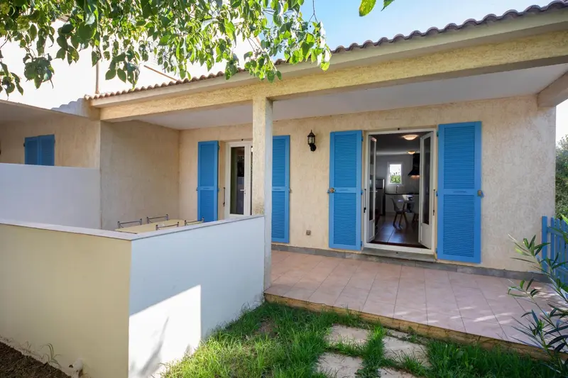 Une terrasse devant une habitation aux volets bleus.