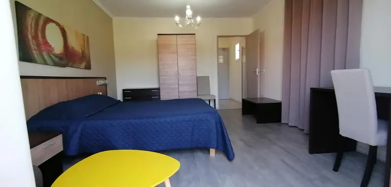 Une chambre lumineuse avec un grand lit recouvert d'une couverture bleue et un bureau.