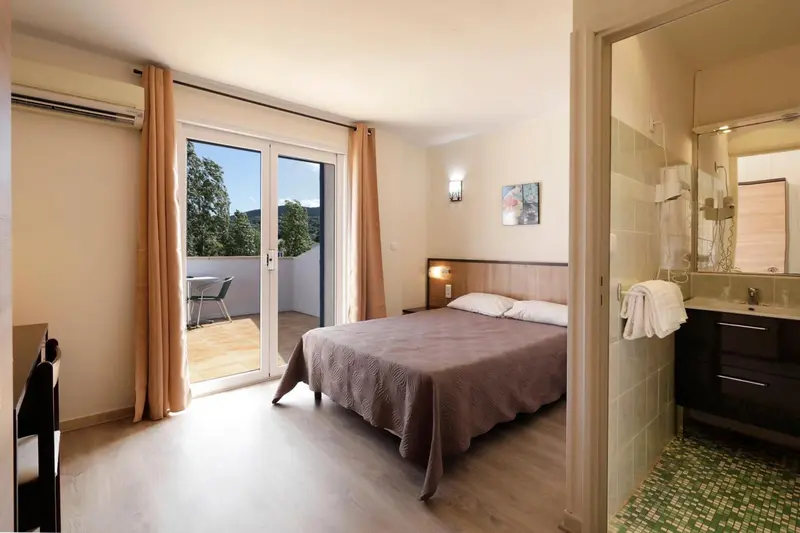 Une chambre lumineuse s'ouvre sur une terrasse avec vue sur la végétation.
