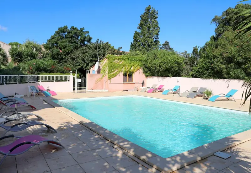 Transats bleus et roses disposés autour d'une piscine ensoleillée.