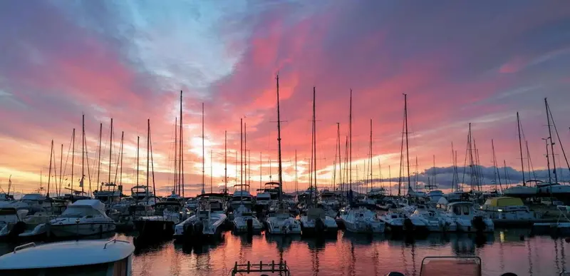 Un coucher de soleil illumine un port de plaisance rempli de voiliers et de bateaux à moteur.