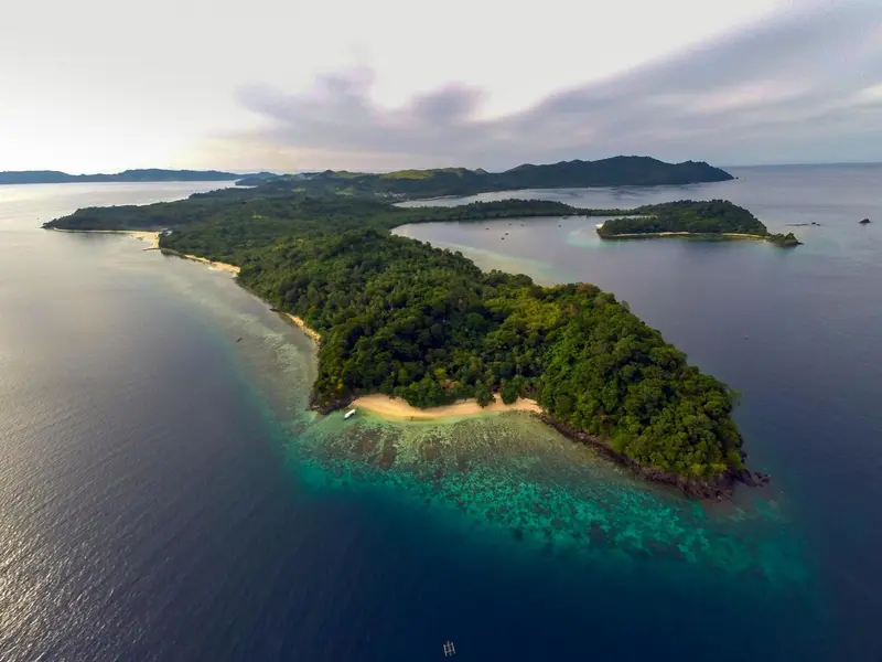 Vue aérienne d'une île tropicale bordée de plages et de végétation luxuriante.