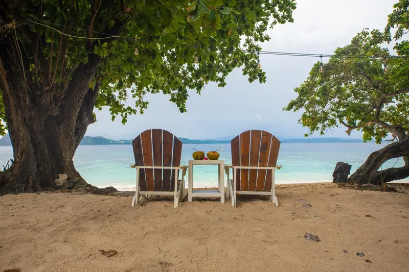 Deux fauteuils en bois face à la mer sur une plage de sable.