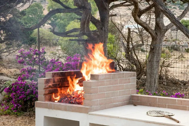 Un barbecue en pierre allumé dans un jardin ensoleillé.