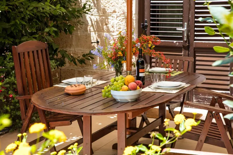 Table en bois dressée avec de la vaisselle et des fruits sur une terrasse ensoleillée.