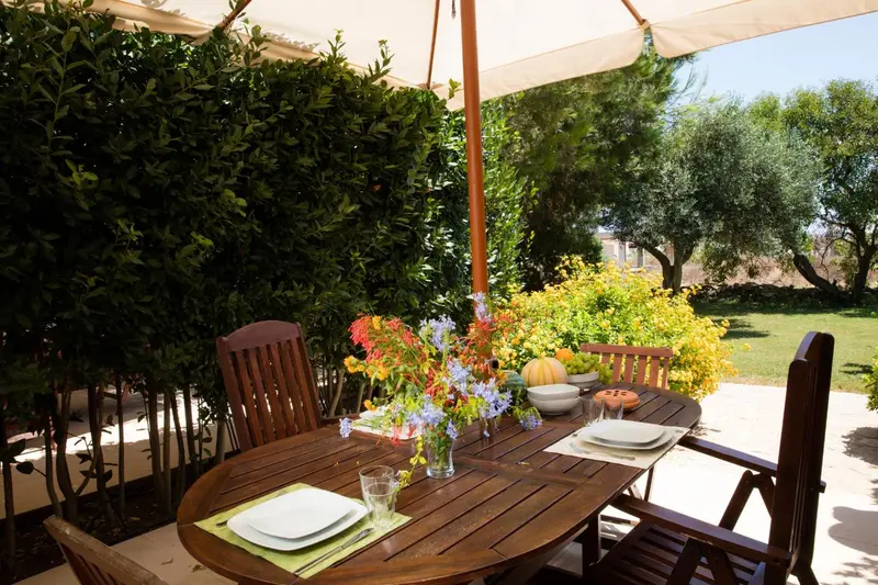 Table en bois dressée pour un repas en extérieur, décorée de fleurs et de fruits.