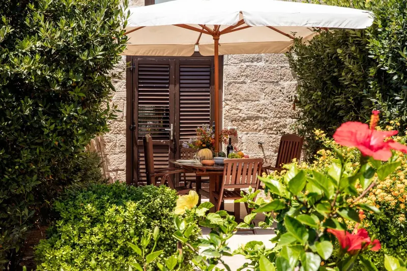 Une table à manger en bois est mise en scène sur une terrasse fleurie.