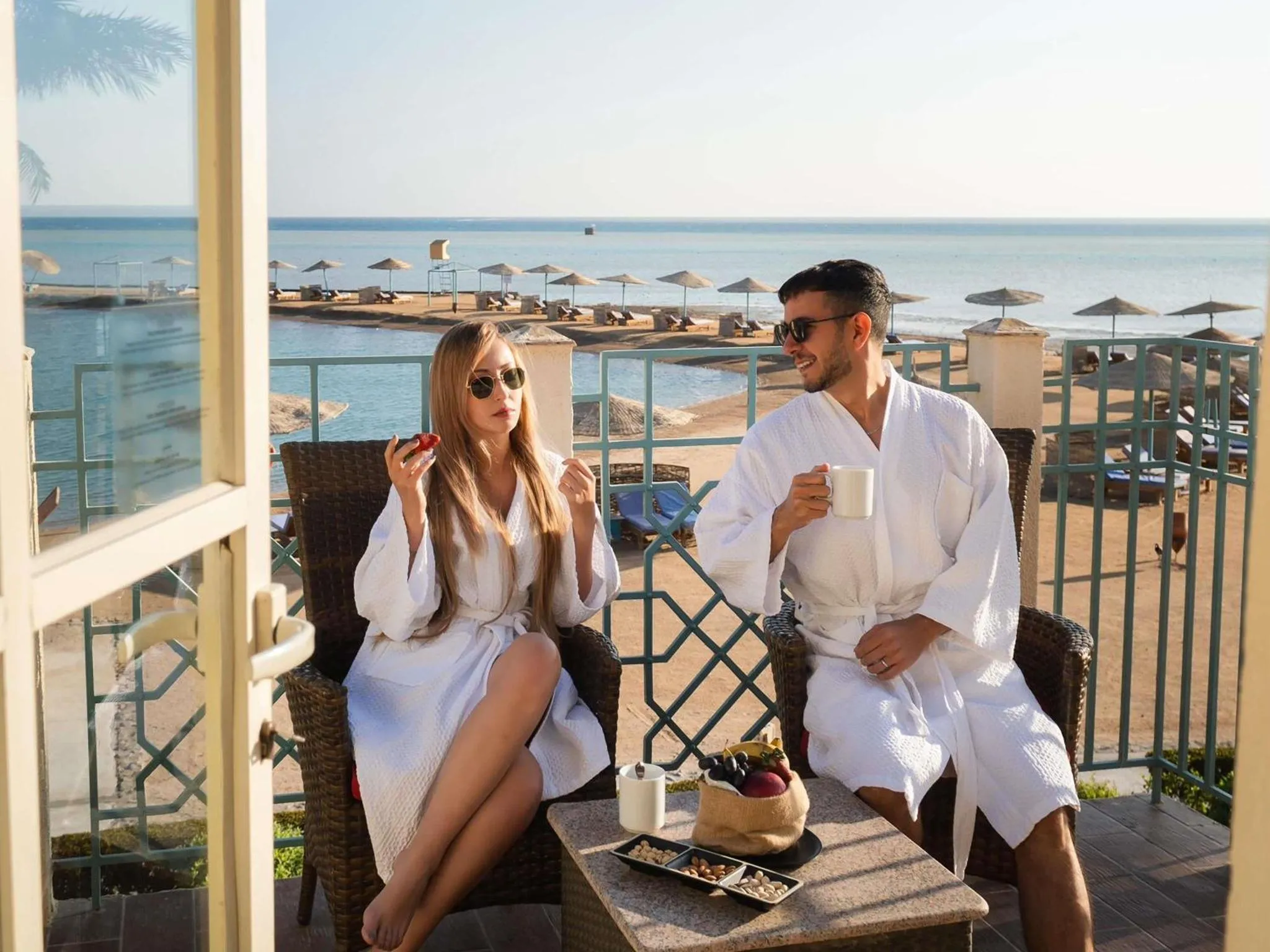 Un couple profite d'un petit-déjeuner sur une terrasse ensoleillée avec vue sur la mer.