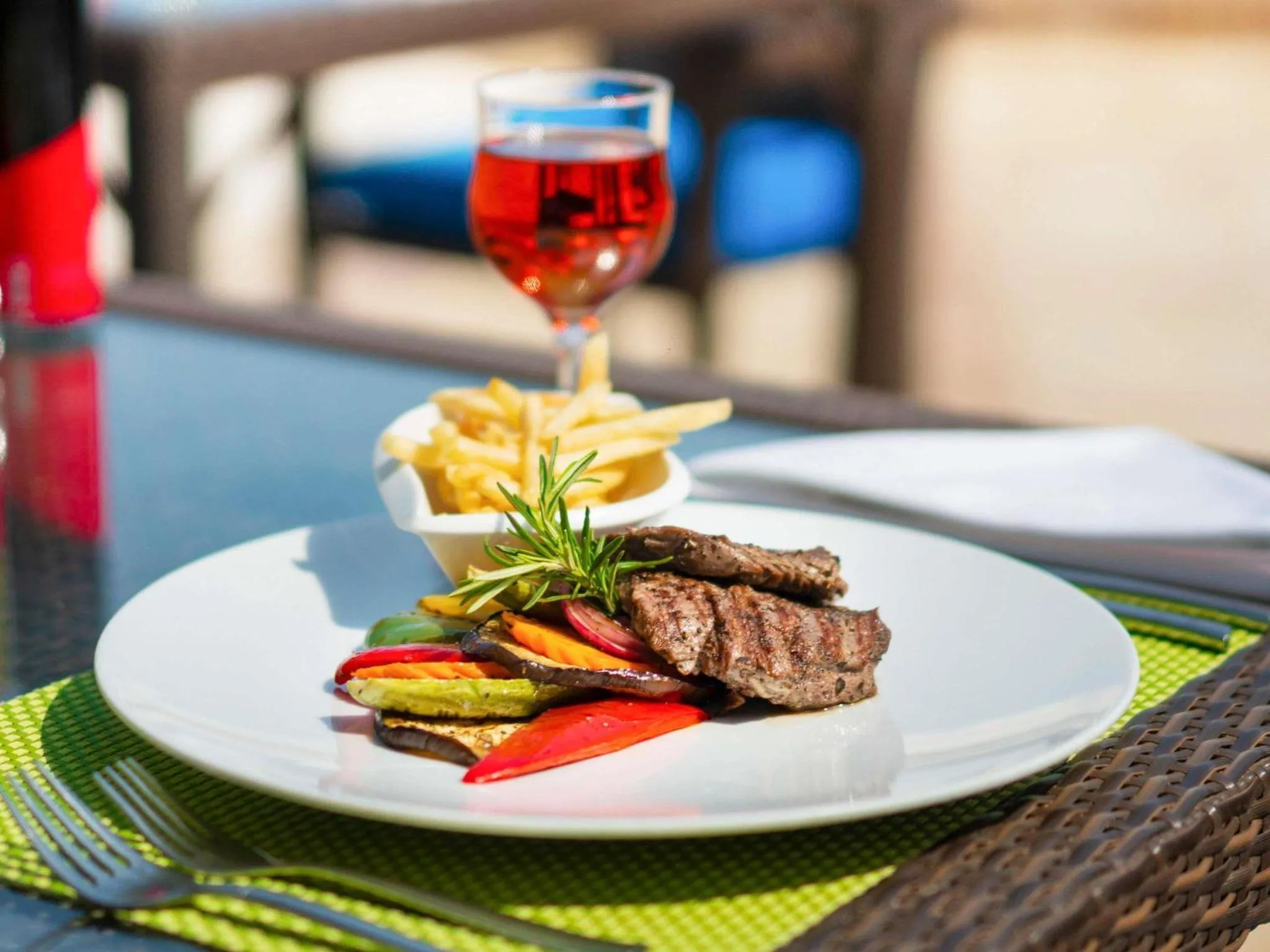 Assiette de viande grillée accompagnée de légumes et de frites, avec un verre de boisson.