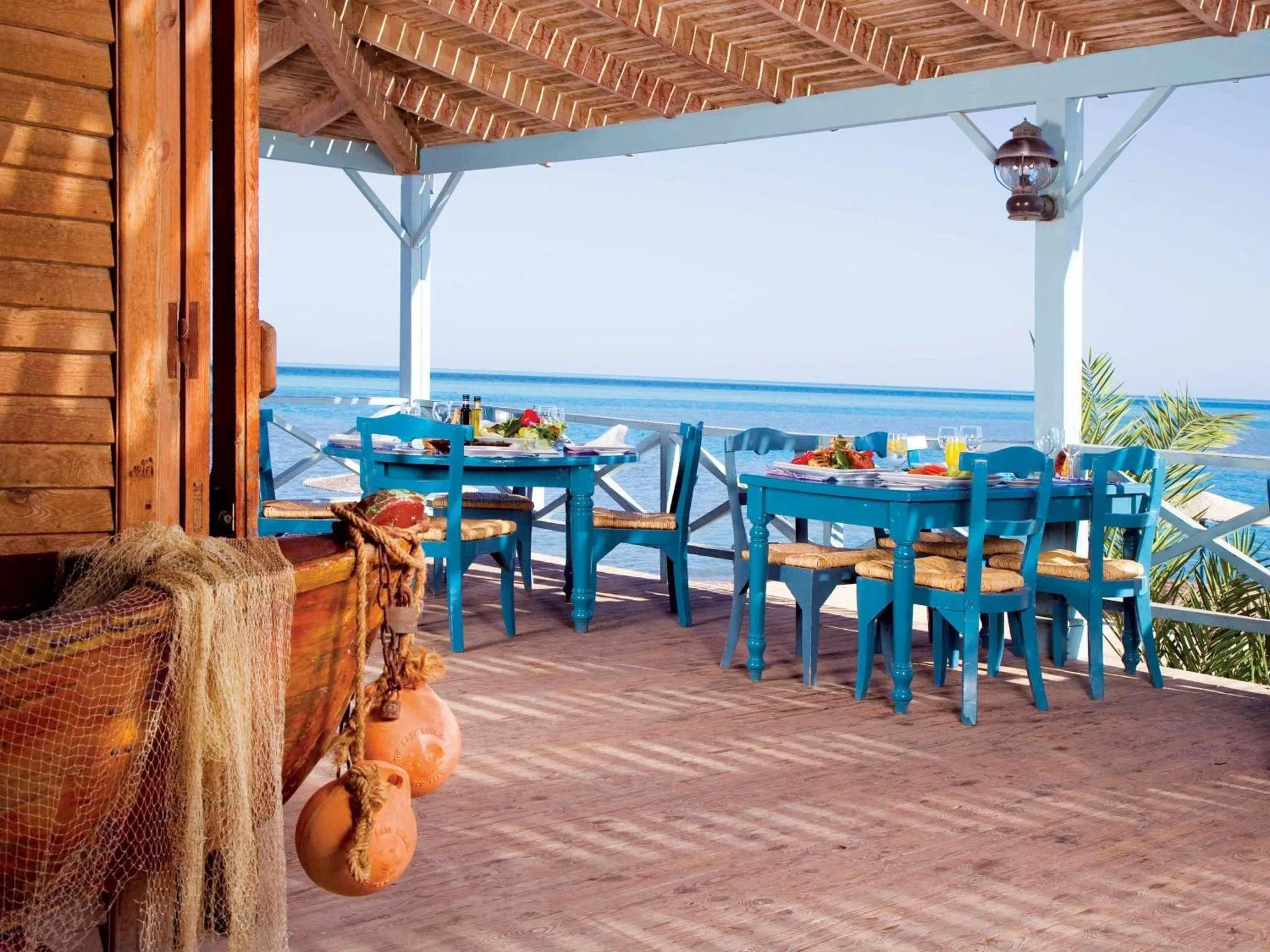 Terrasse ombragée avec tables et chaises donnant sur la mer.